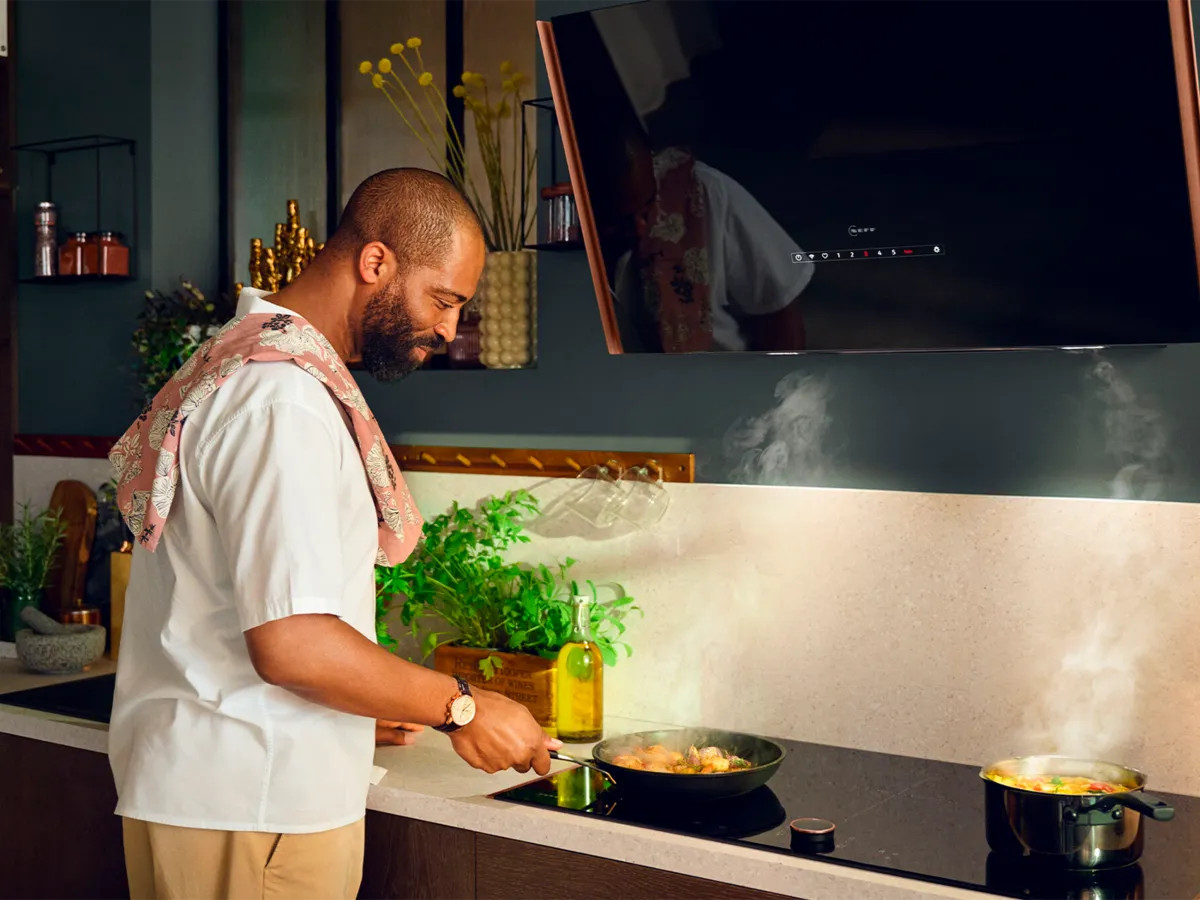 Un uomo sta preparando una pietanza in cucina assistito dalla cappa inclinata NEFF.