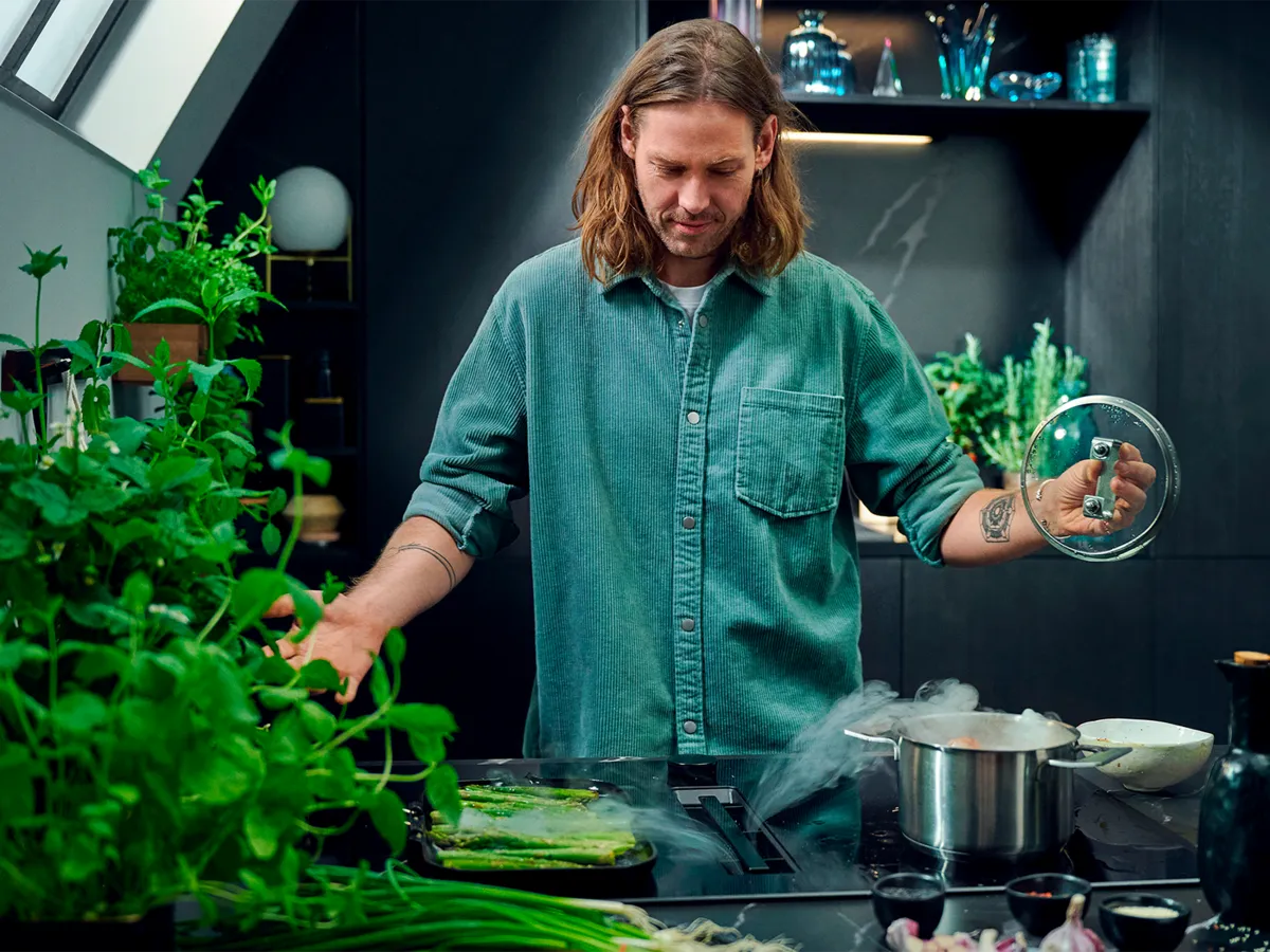 Man in black kitchen, opening pot, steam is getting drawn into venting cooktop