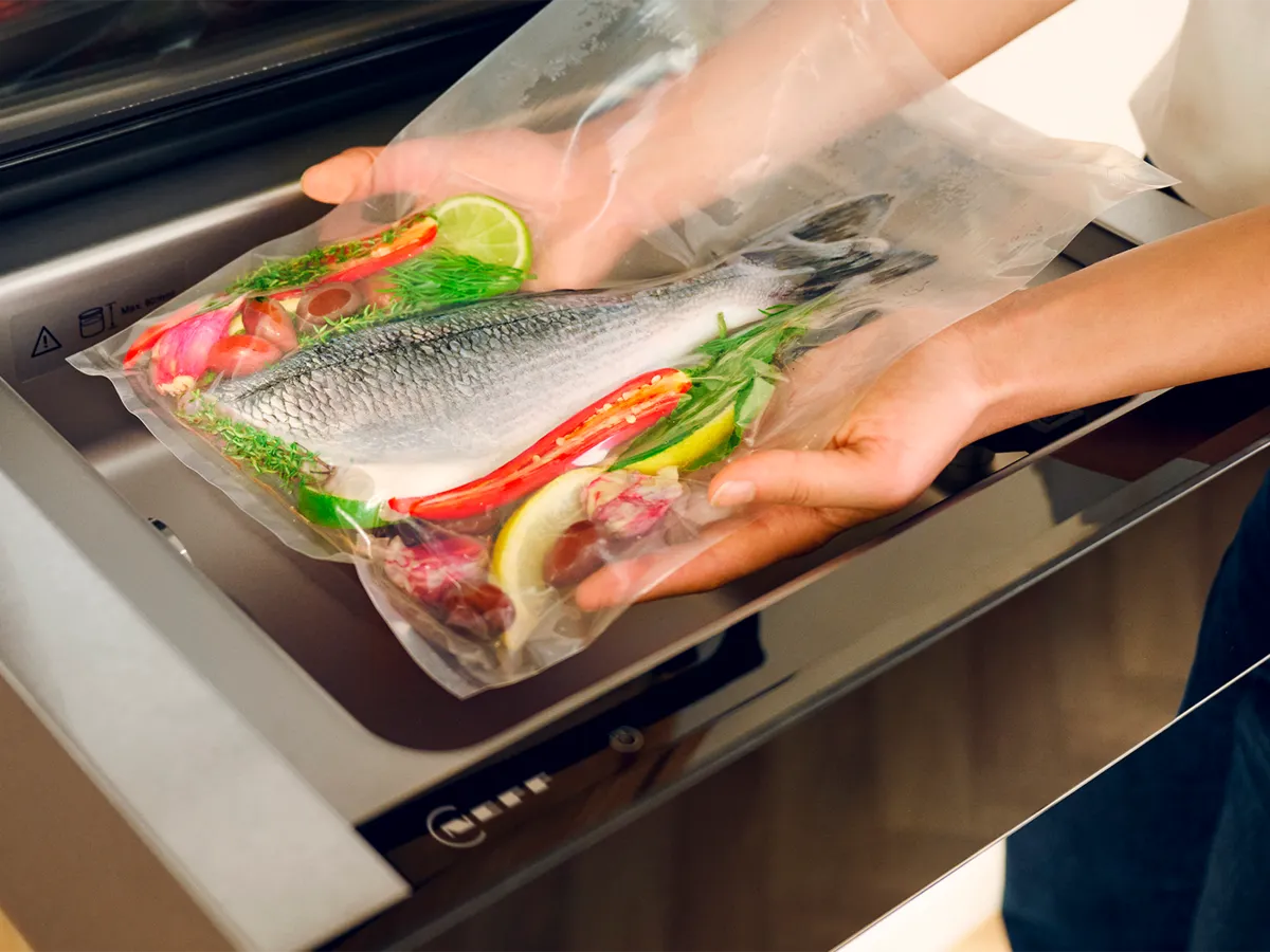 A closer view inside a Sous-vide Drawer beneath an oven into which a person is placing a sous-vide bag with prepared food