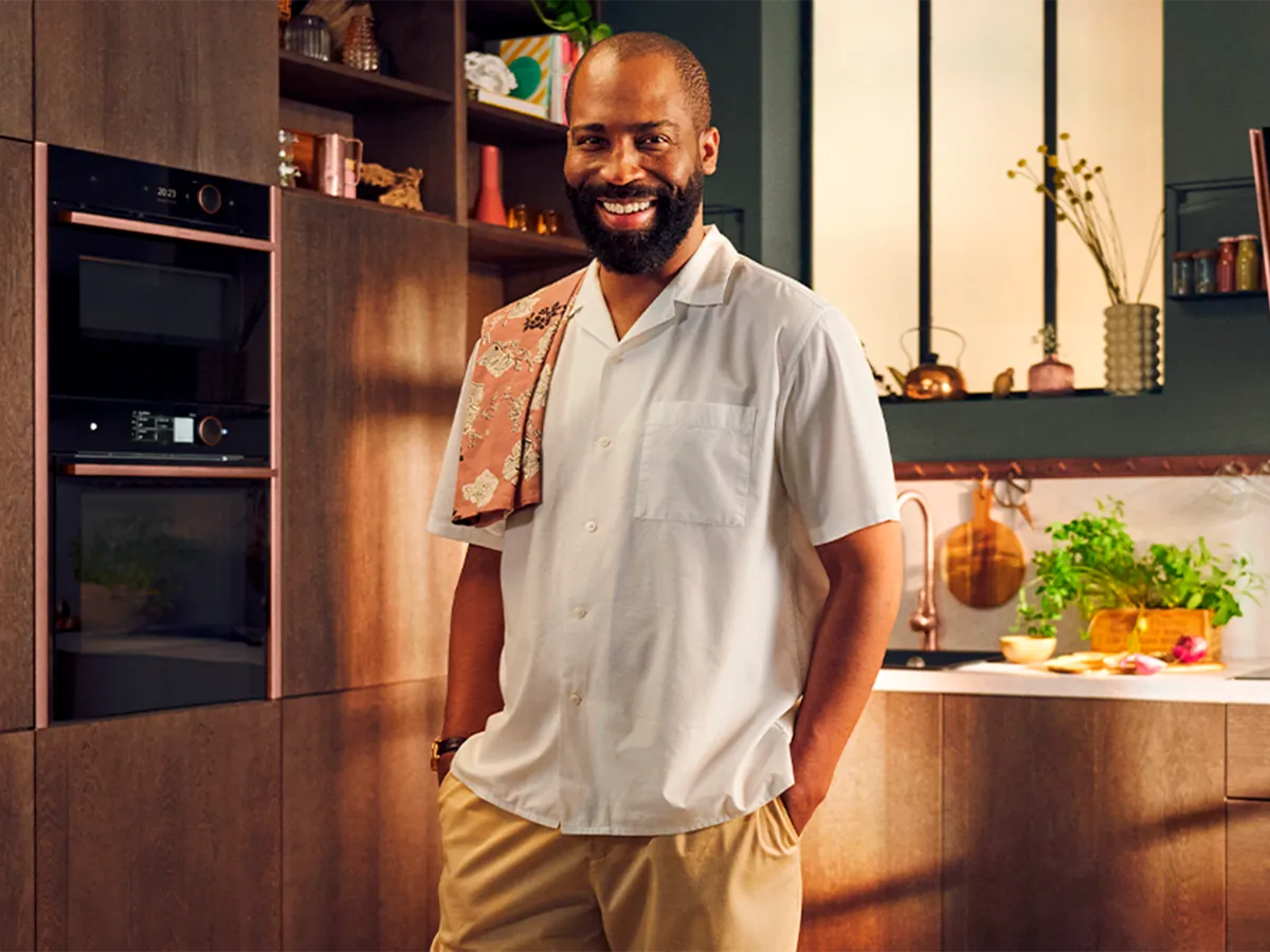 Un uomo in piedi in una cucina marrone, vicino al forno e al microonde integrati NEFF.