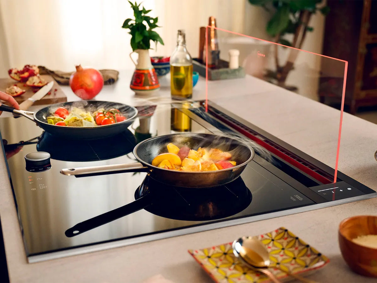Glass draft hood shown with various dishes cooking on hob 