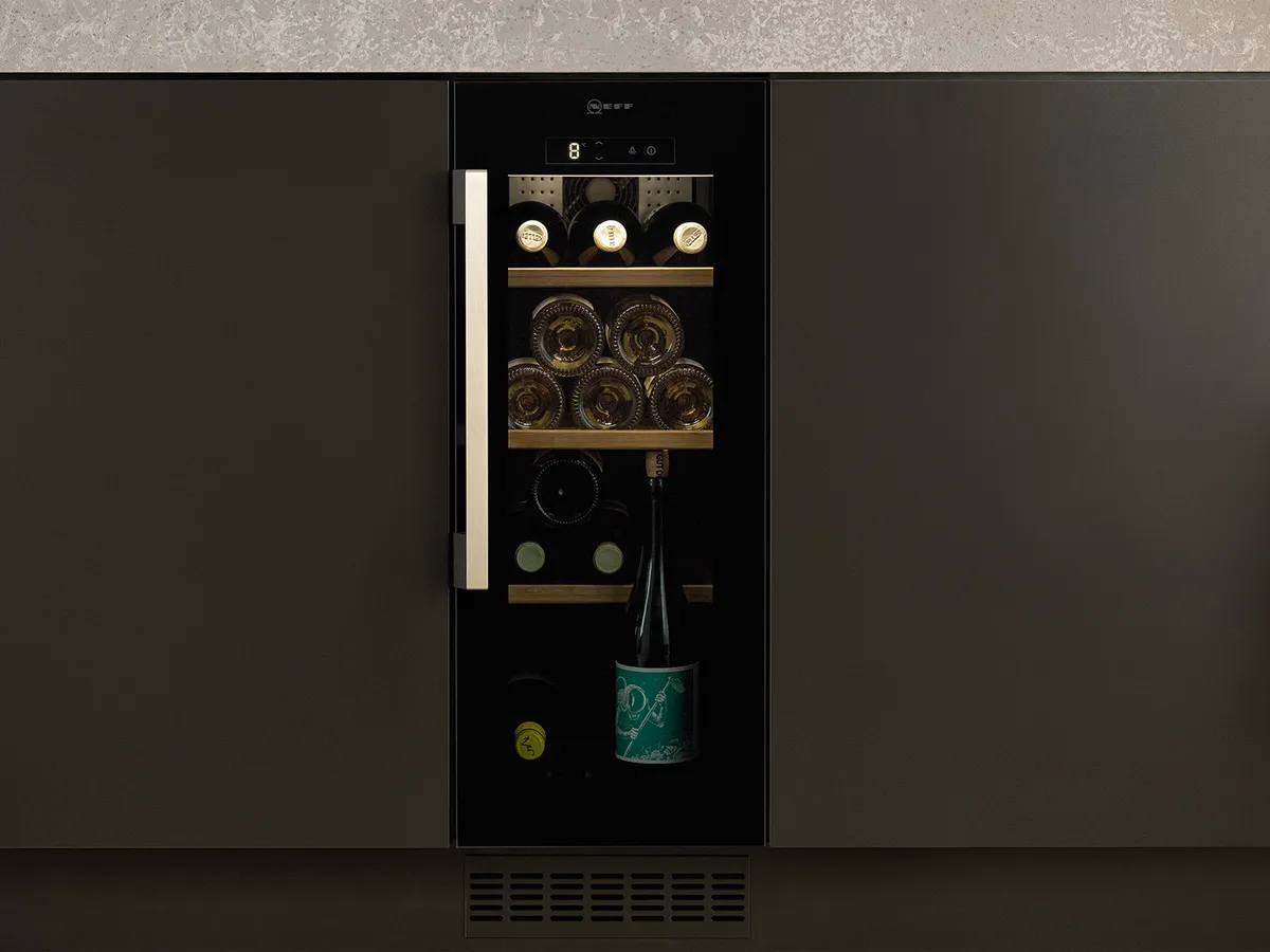 A narrow wine cooler half the width of a kitchen cupboard, integrated underneath a kitchen island.