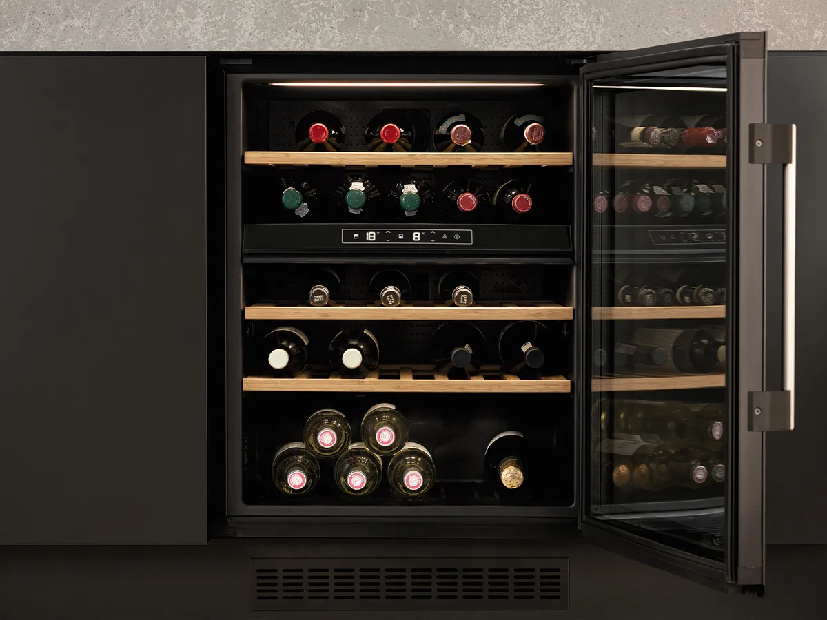 An open wine cooler with multiple bottles inside, underneath a kitchen island.