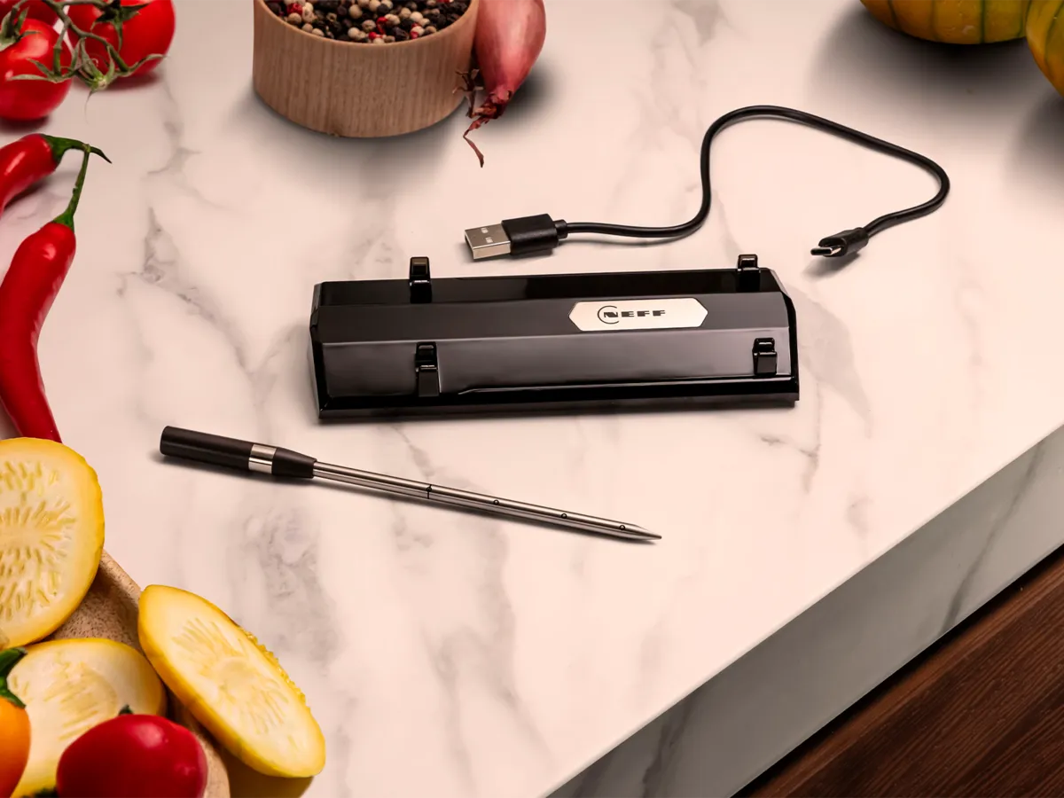 Stiilne must NEFF-i lihaandur, mille kõrval asetsevad värsked köögiviljad marmorist köögitasapinnal. 