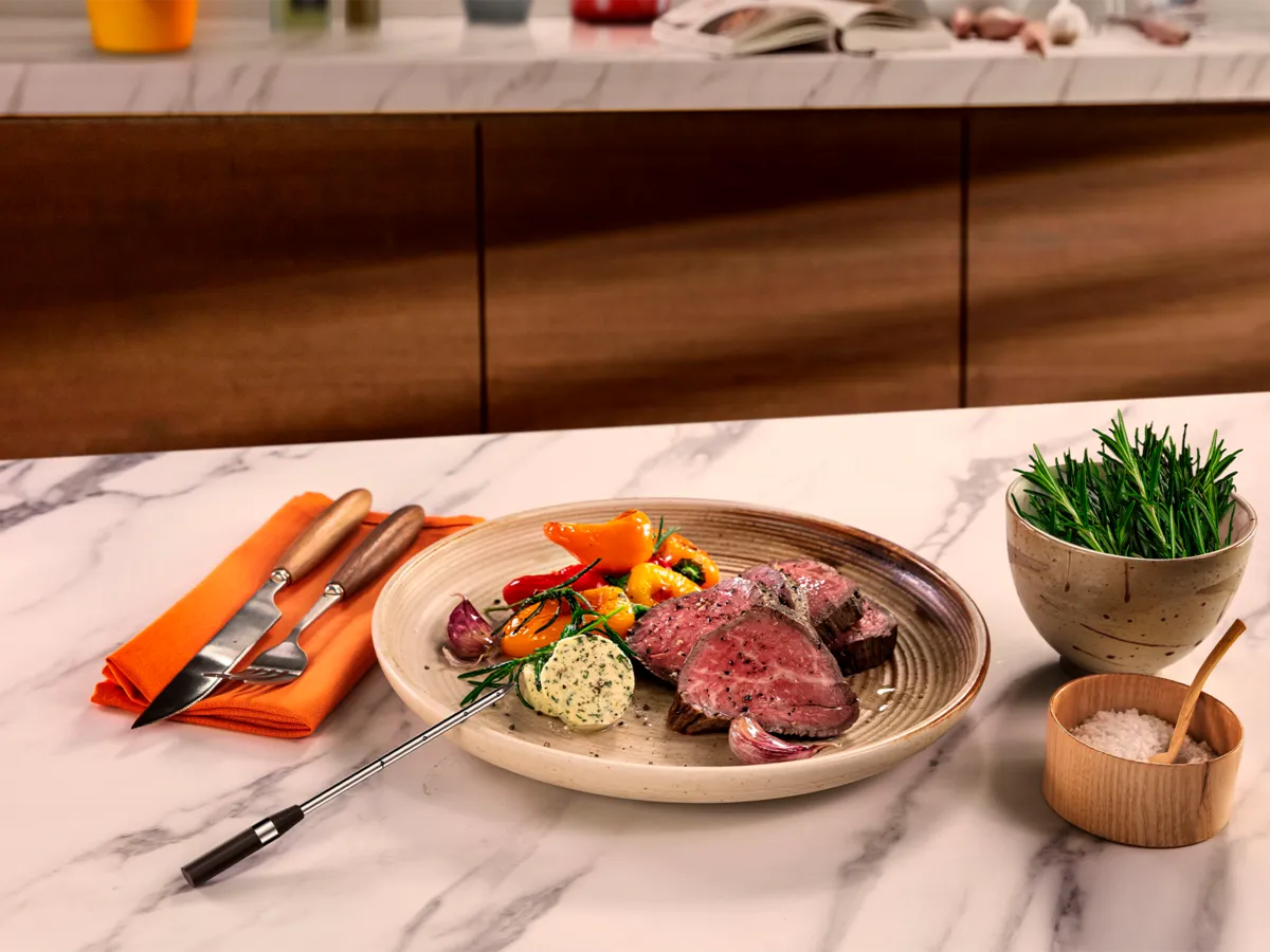 Taldrik täiuslikult küpsetatud veiseliha, köögiviljade ja ürdivõiga marmorist tööpinnal.