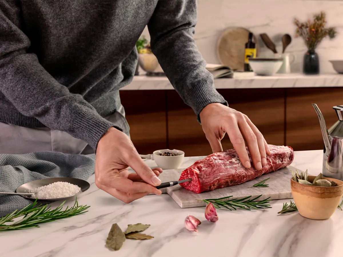 Hallis kampsunis inimene valmistab marmorist tööpinnal ette toorest lihatükki, sisestades sellesse NEFF-i lihaanduri.