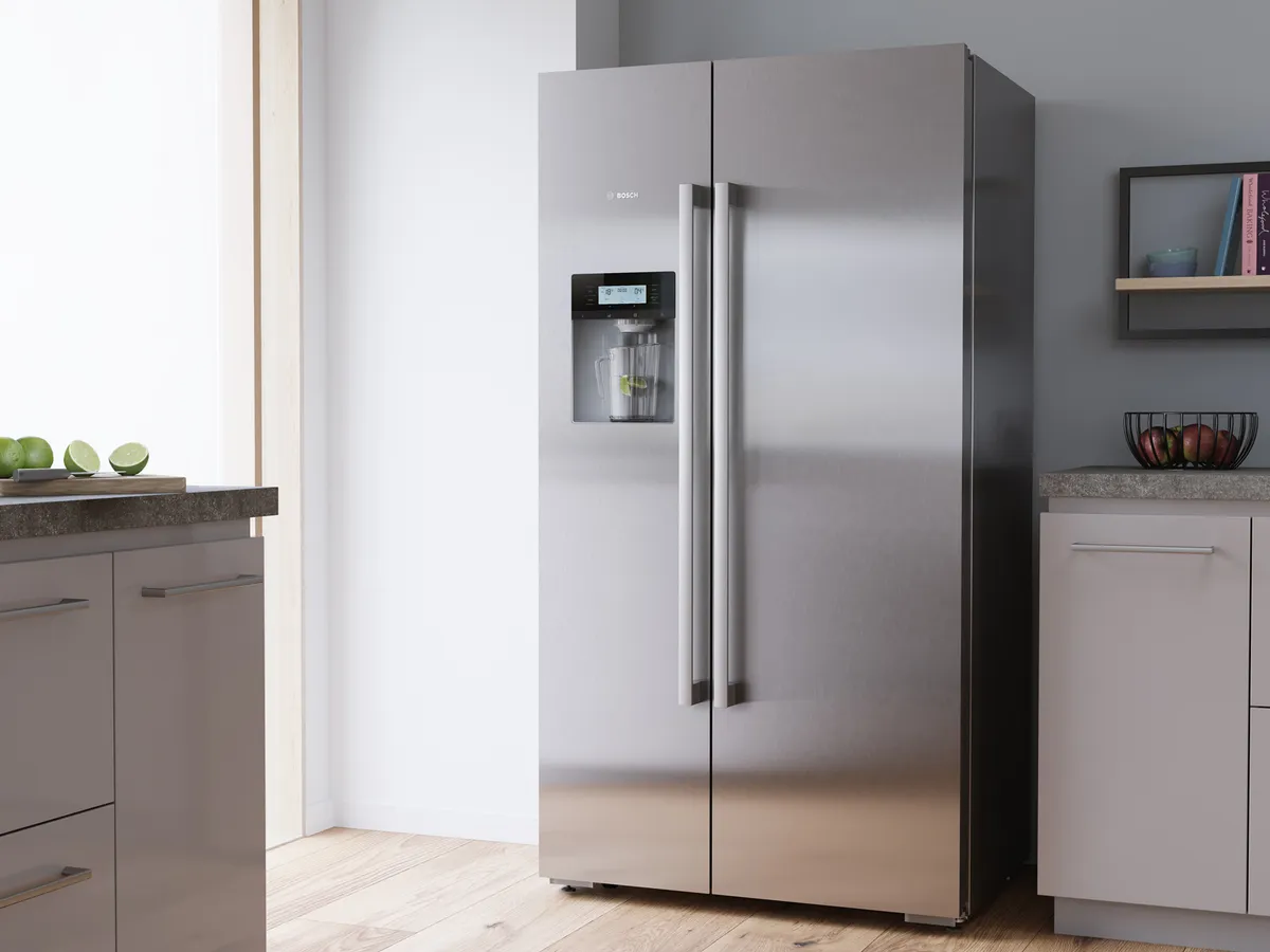 Um frigorífico em aço inoxidável está situado numa cozinha moderna ao lado de uma bancada com limas verdes e uma tigela de frutas.