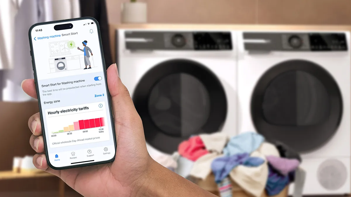 Smartphone visar energianvändningsdata, tvättmaskiner i bakgrunden, tvätthög synliga.
