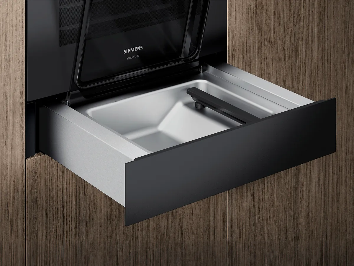 A sleek, Siemens vacuum drawer in black and stainless steel, partially open, set against a wooden background.
