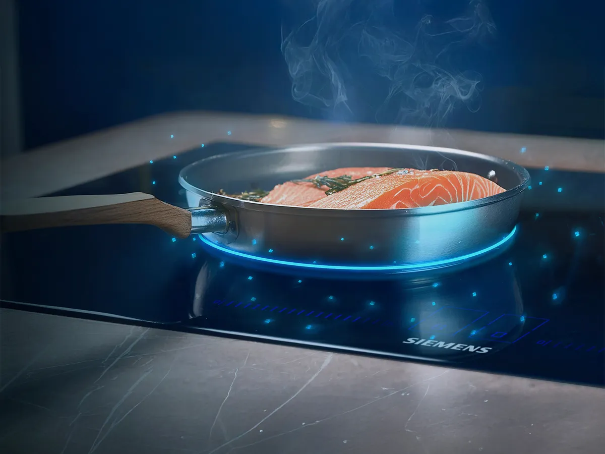 Uma frigideira com filetes de salmão crus numa placa de indução moderna, rodeada de efeitos de luz e vapor, indicando a cozedura.
