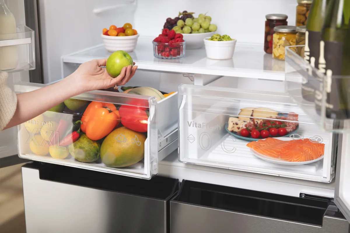A person opens a Bosch French door fridge freezer, revealing various food items and beverages inside.