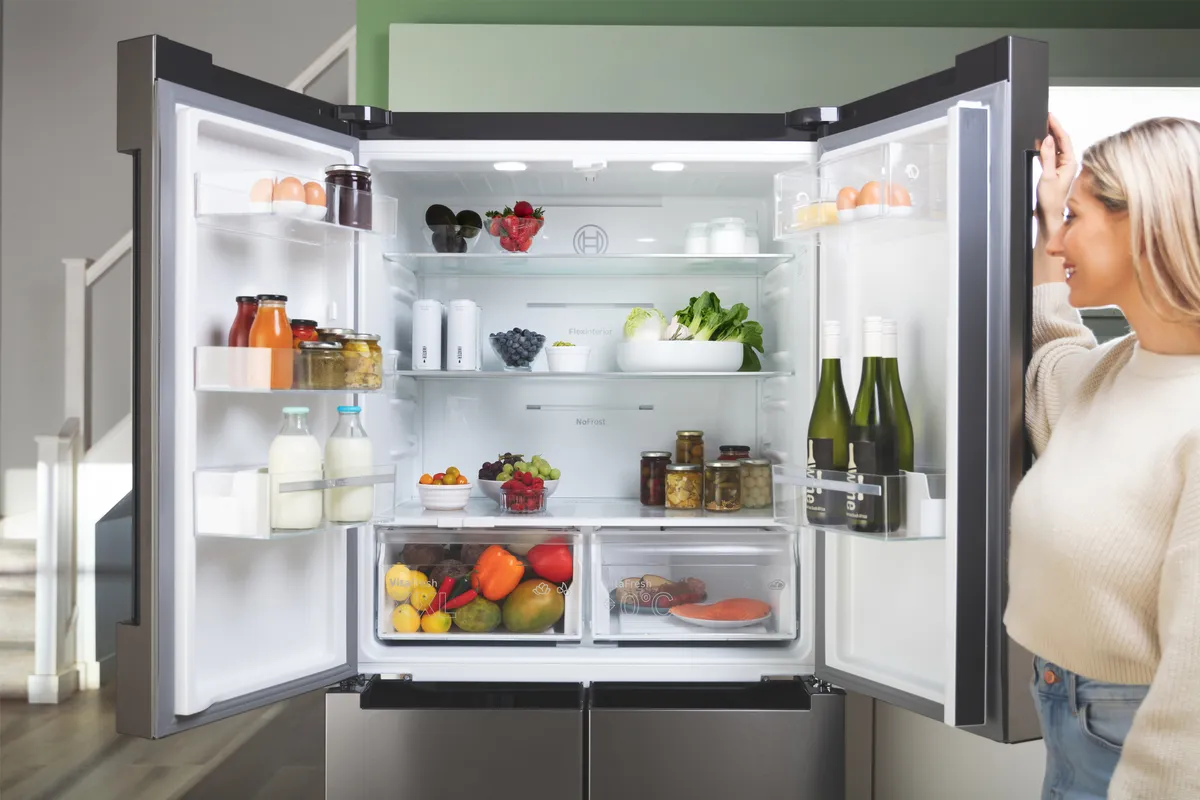 A woman examines the interior of a Bosch multi-door fridge freezer, showcasing its organized shelves and compartments.