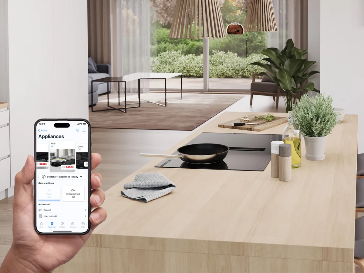 Uma cozinha moderna com uma placa de indução numa ilha. Pessoa segurando um smartphone que mostra um aplicativo.