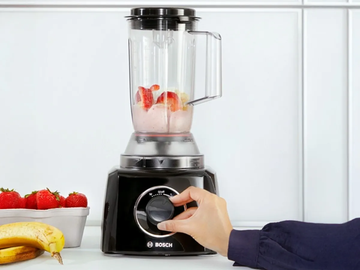 Uma pessoa ajusta o botão de um liquidificador Bosch cheio de frutas.
