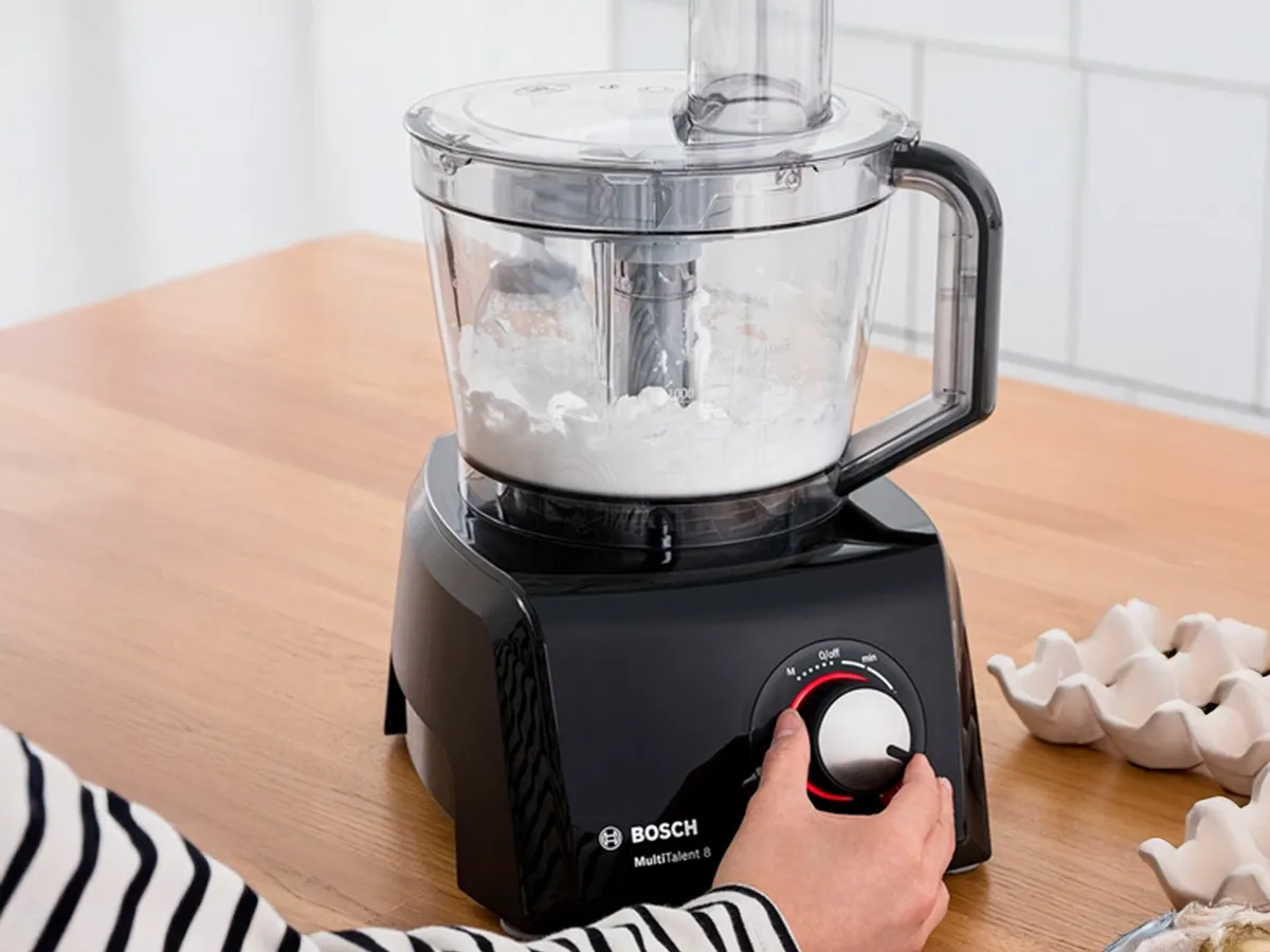 Uma pessoa ajusta o botão de controlo num processador de alimentos MultiTalent 8, misturando ingredientes numa tigela.