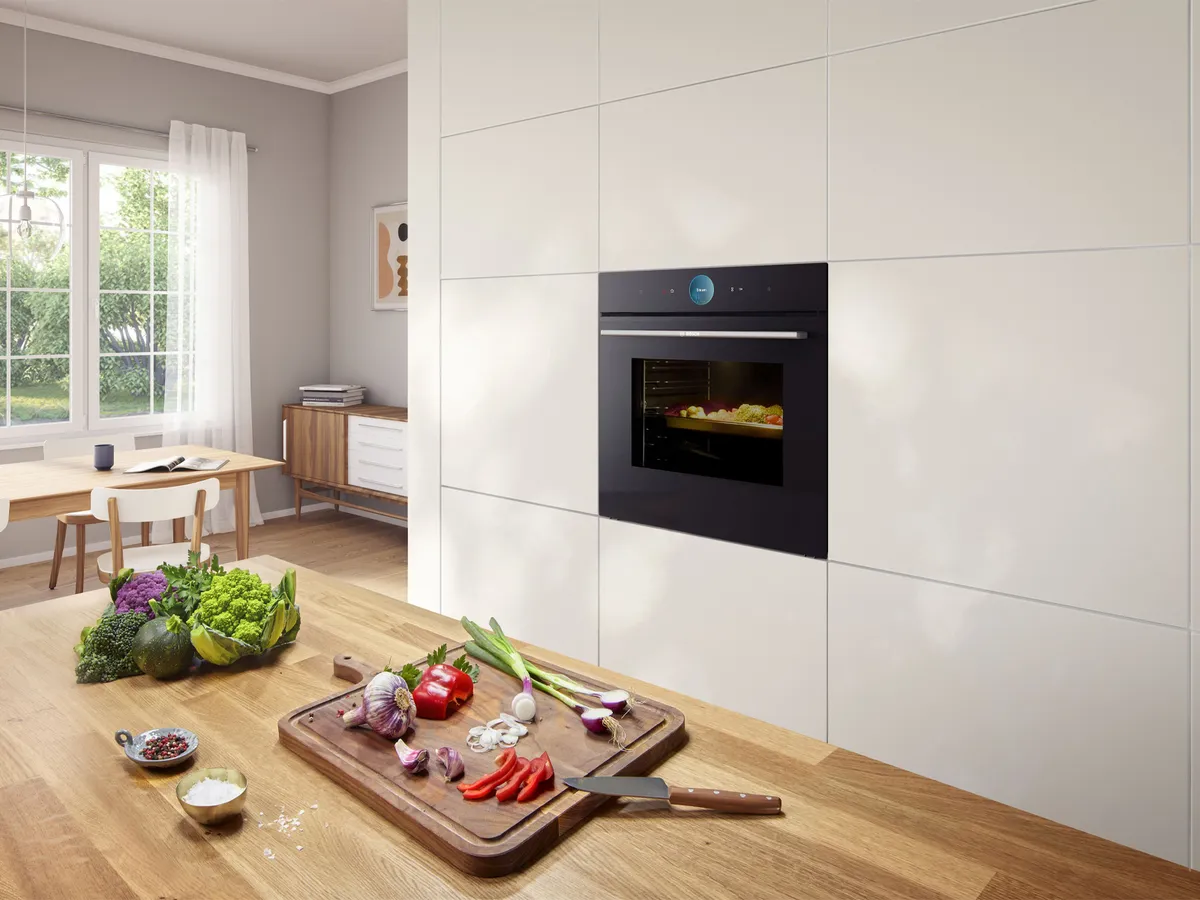 Uma cozinha moderna com forno embutido e vegetais frescos numa tábua de cortar de madeira.