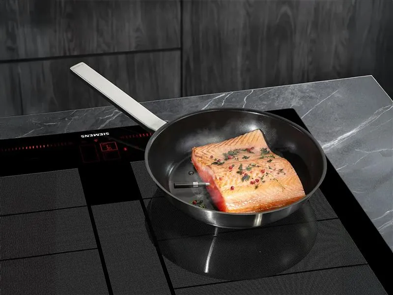 En laxfilé med en trådlös roastingSensor insatt, som steks i en panna på en Siemens spishäll.