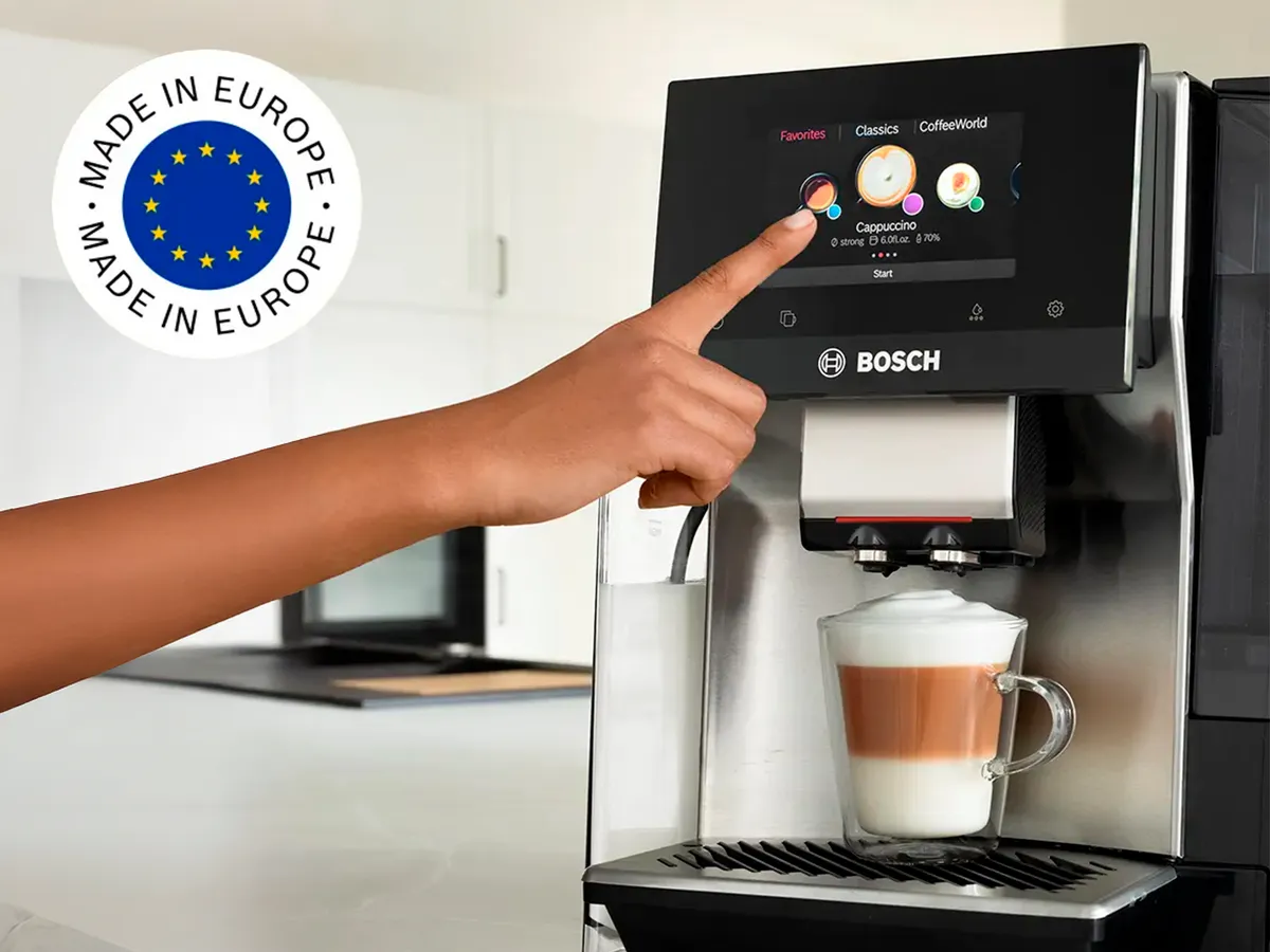 Pessoa a pressionar o ecrã tátil da máquina VeroCafe Série 8, com a bandeira da Europa no canto superior da imagem.