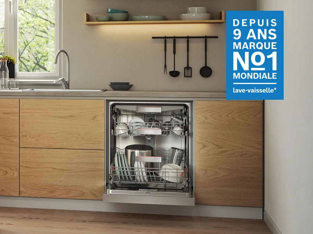 Une cuisine moderne comporte un lave-vaisselle Bosch ouvert rempli de vaisselle, ainsi qu'un comptoir en bois et un panneau promotionnel bleu.