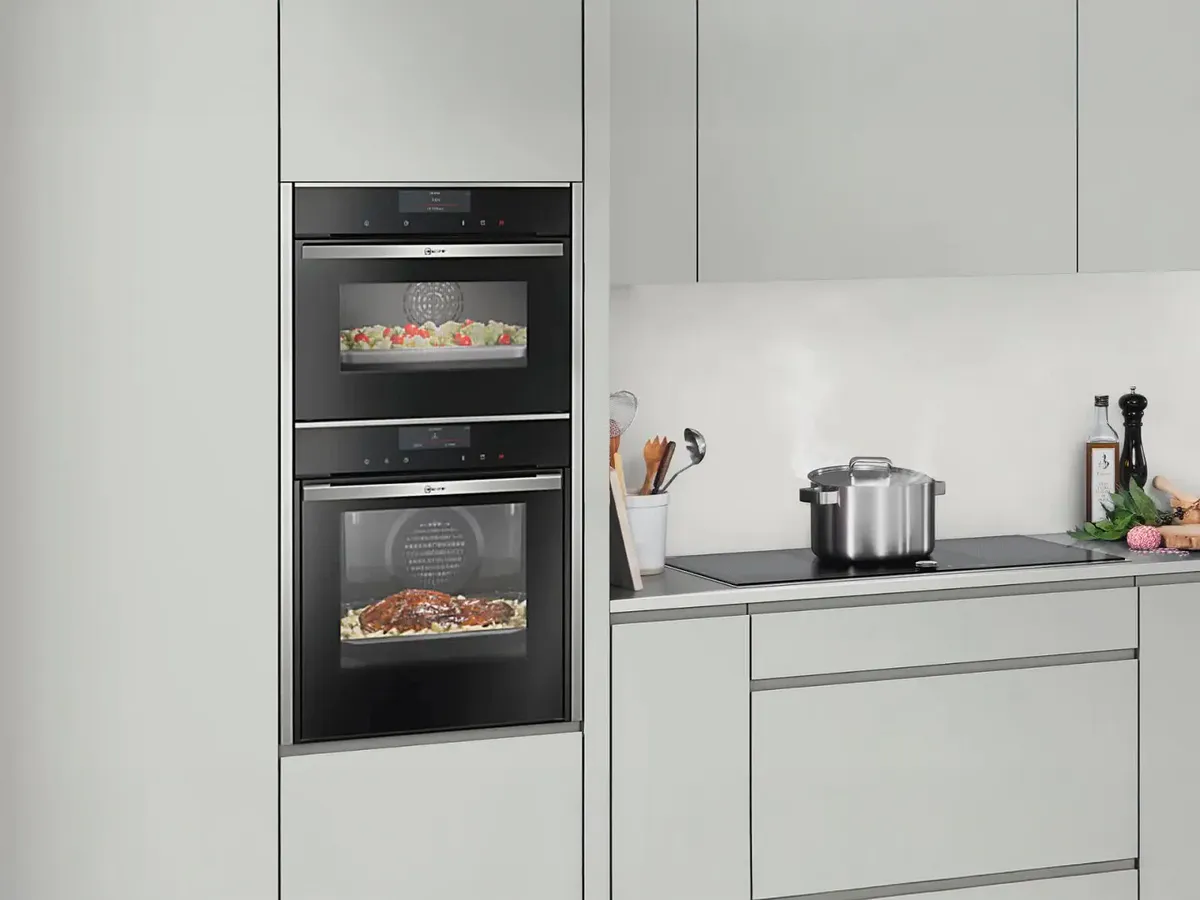 Moderne Küche mit doppeltem Backofen, Gemüseplatte, Bratentopf und Dampfkochtopf auf einer glatten Arbeitsplatte.