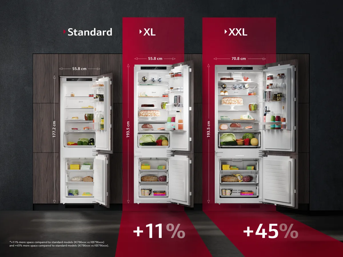 An open built-in fridge freezer inside a light-wood kitchen illuminated by daylight.