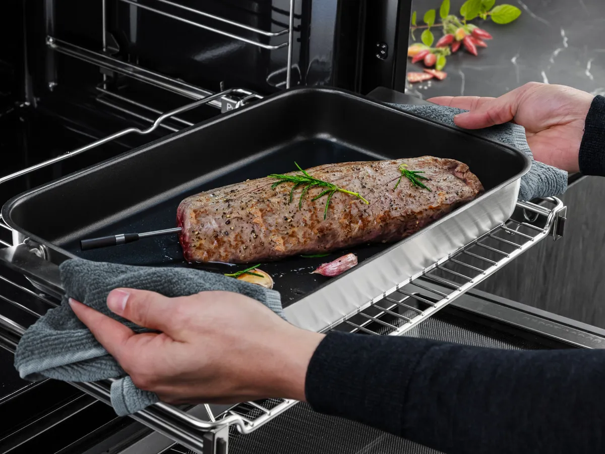 Två händer som tar ut en tillagad rostbiff med den trådlösa roastingSensor insatt från ugnen.