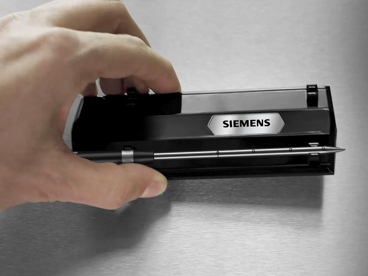 En hand håller den trådlösa rostsensorns laddningsstation med sensorsnålen fastklämd.