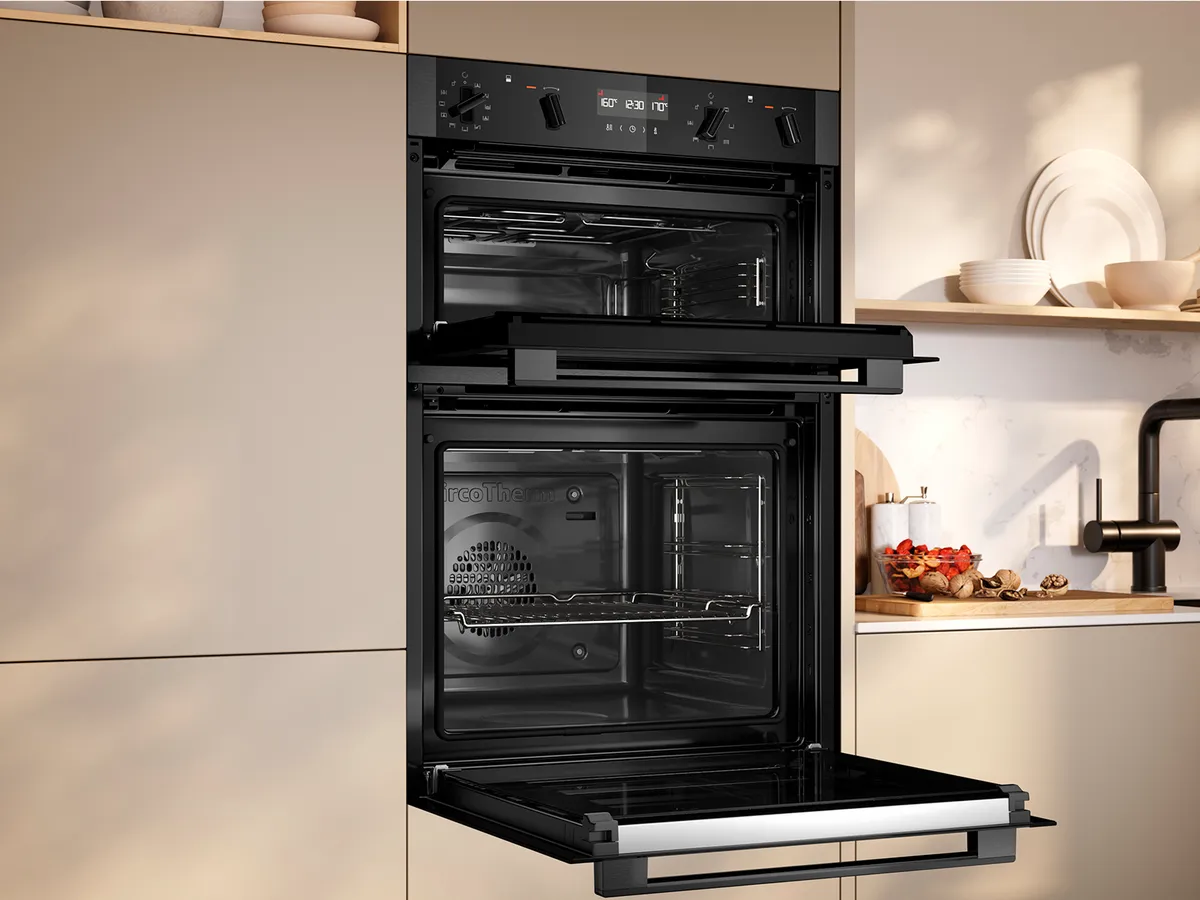 A double oven built into a kitchen cabinet, featuring two open doors, a digital control panel, and a minimalist design.