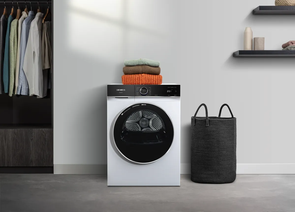 Ein moderner weißer Trockner mit ordentlich gestapelten Handtüchern oben, in einem stilvollen Wäscheraum neben einem schwarzen Wäschekorb und einem Schrank.