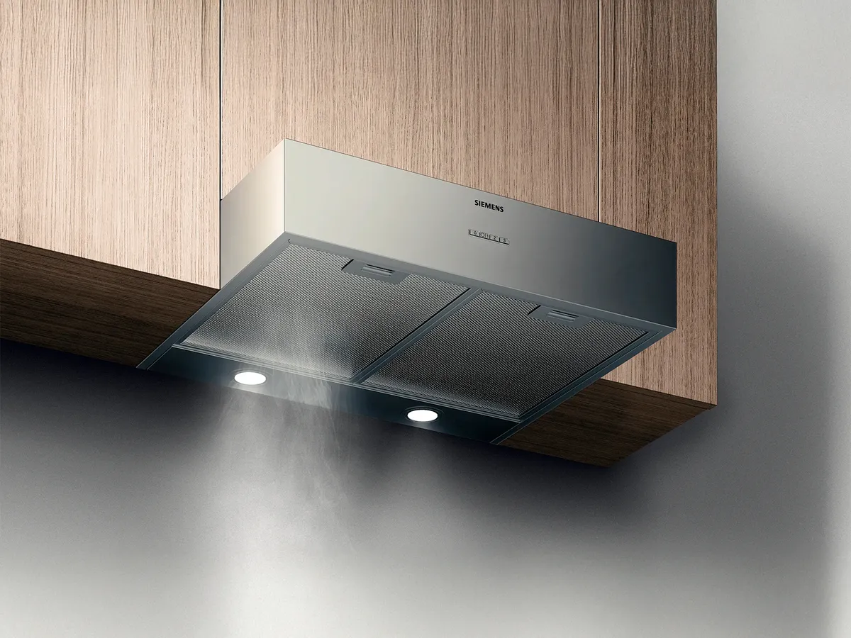 A sleek Siemens kitchen hood mounted under cabinetry, releasing steam with built-in lights for enhanced visibility during cooking.