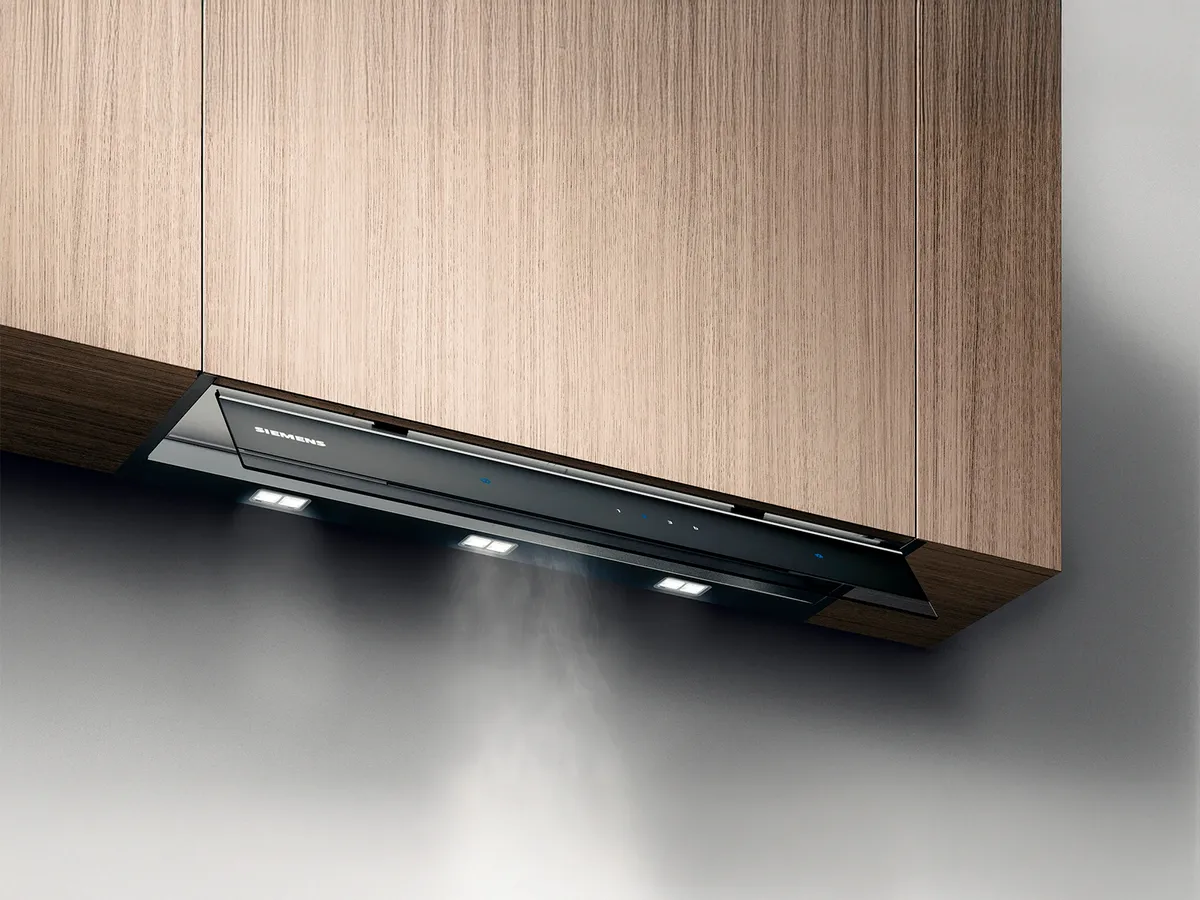 Uma chaminé Siemens elegante instalada sob os armários de madeira, emitindo vapor com luzes embutidas iluminando a área de cocção.