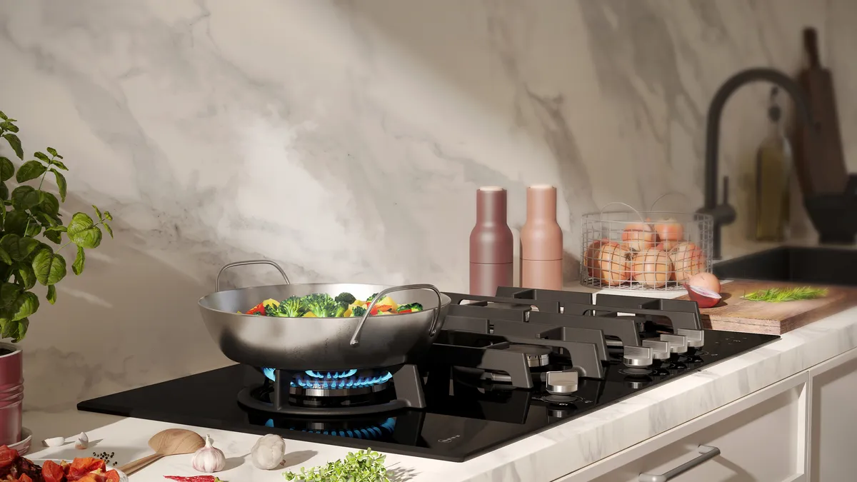 Eine moderne Küche mit einem Wok mit buntem Gemüse auf einem Gasherd, frischen Zutaten und stilvoller Dekoration vor einem Marmorhintergrund.