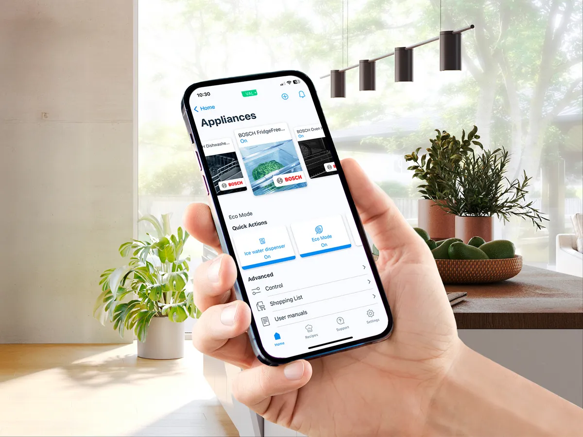 En hand som håller i en smartphone som visar en app för hushållsapparater, med alternativ för att styra enheter.