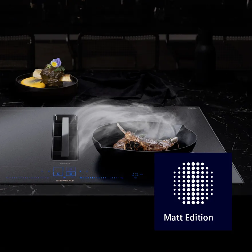 Elegante Küchenumgebung mit einer rauchenden Gusseisenpfanne mit Steak neben einem stilvollen Gericht, präsentiert mit dem Matt Edition Logo.