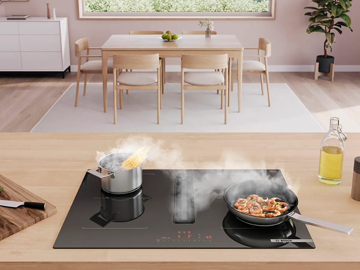 Uma cozinha moderna, com massa a ferver e camarões a crepitarem numa placa de indução.
