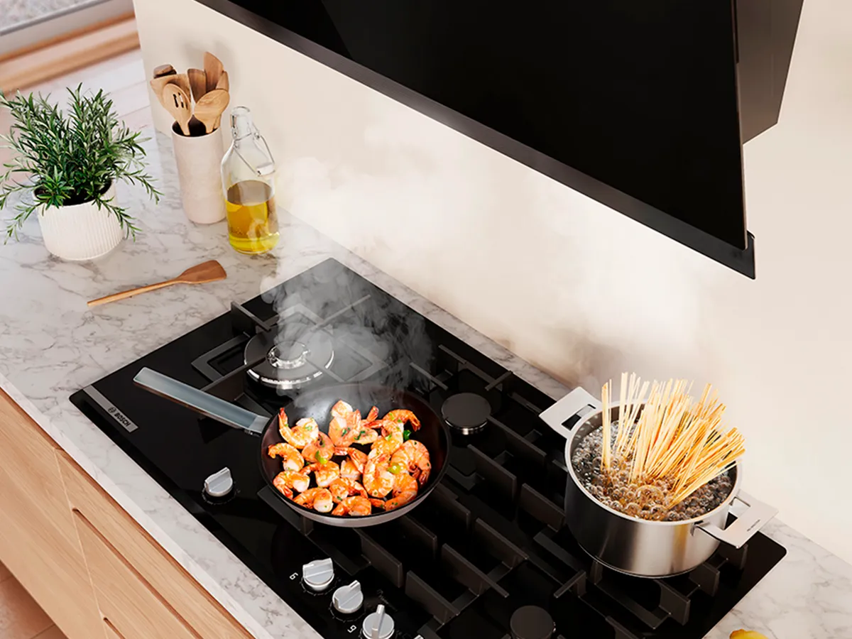 Uma cozinha moderna com um fogão a gás preto, salteando camarões numa panela e fervendo massa numa outra panela.
