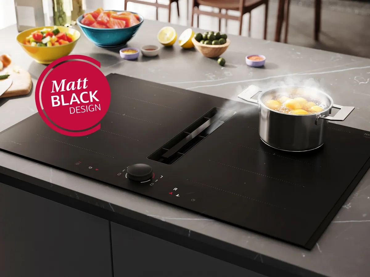 NEFF Induktionskochfeld mit integriertem Dunstabzug im Matt Black Design, Topf mit Dampf, zentrale Absaugöffnung und Twist Pad Flex® Bedienknopf sichtbar.
