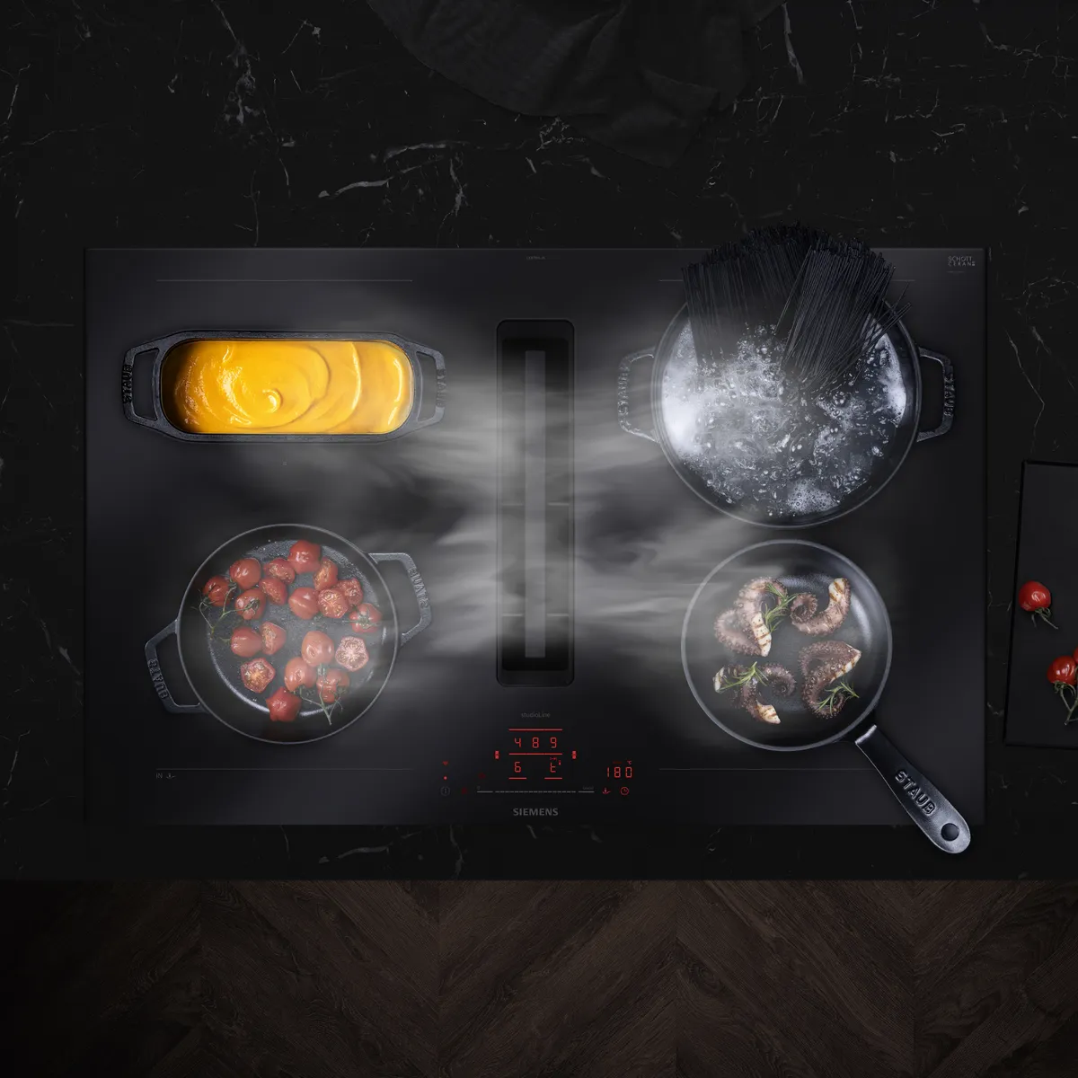 Placa de indução Siemens com tachos e panelas a vapor, mostrando os alimentos a serem cozinhados.