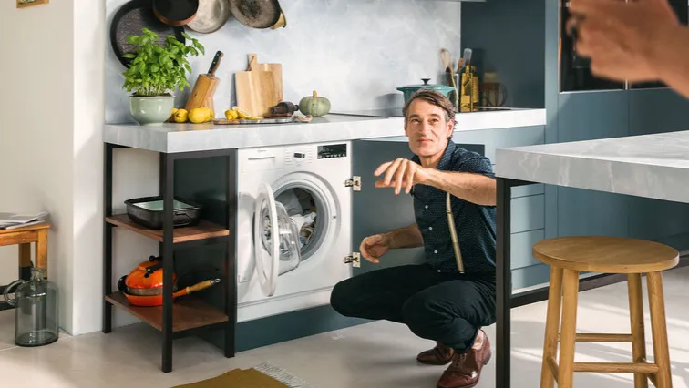 A man kneels in front of a washing machine, preparing to load laundry.