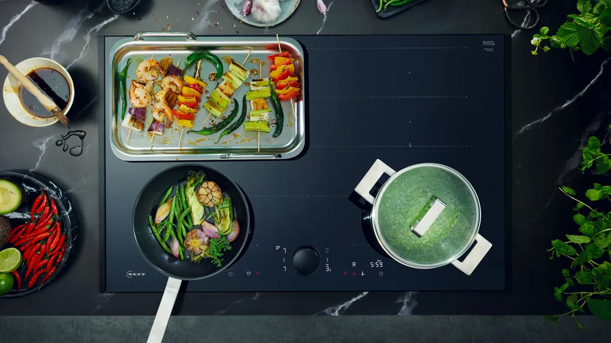 A kitchen featuring induction hobs with a pan cooking food on the stove top.
