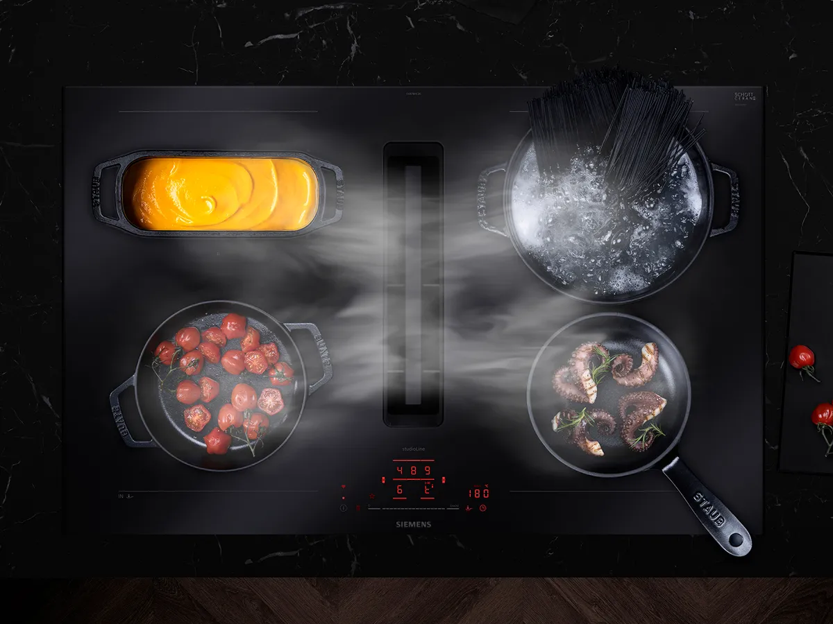 Table de cuisson à induction Siemens avec des casseroles et poêles dégageant de la vapeur, montrant des aliments en train de cuire.