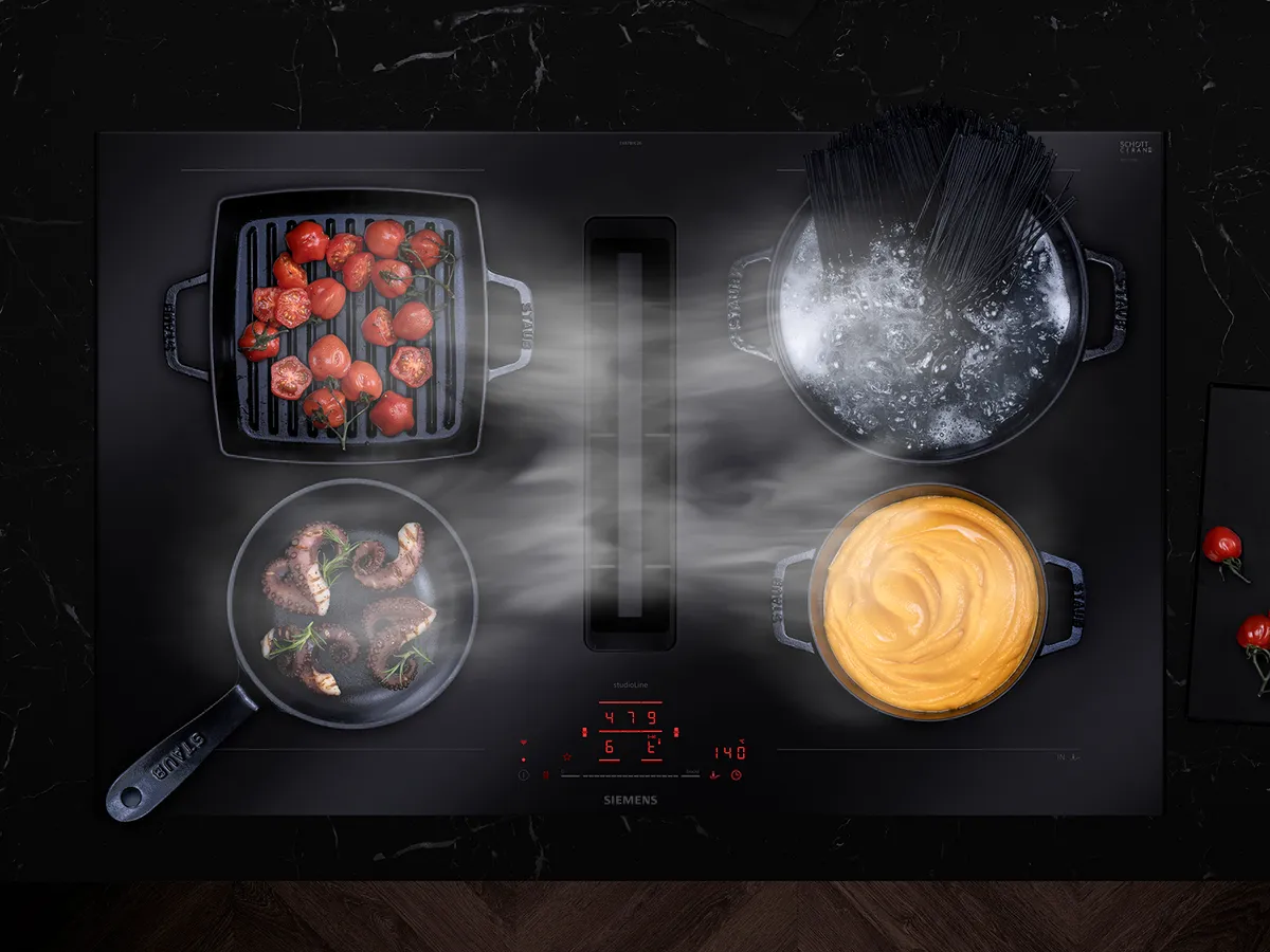 Siemens stove with multiple dishes cooking: tomatoes, pasta, meat, and sauce on black surface.