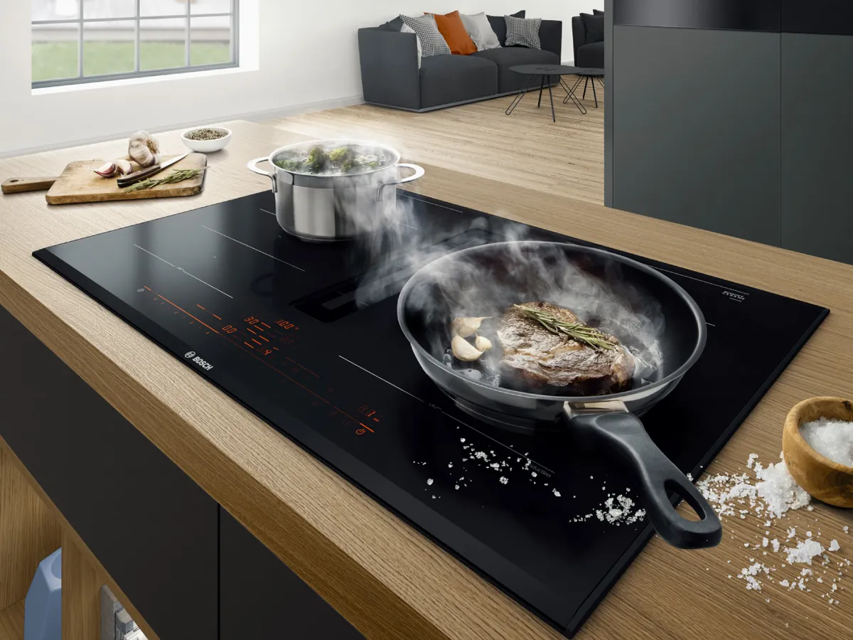 Moderne Küche mit Induktionskochfeld, Kochutensilien und im Hintergrund ein gemütlicher Wohnbereich.