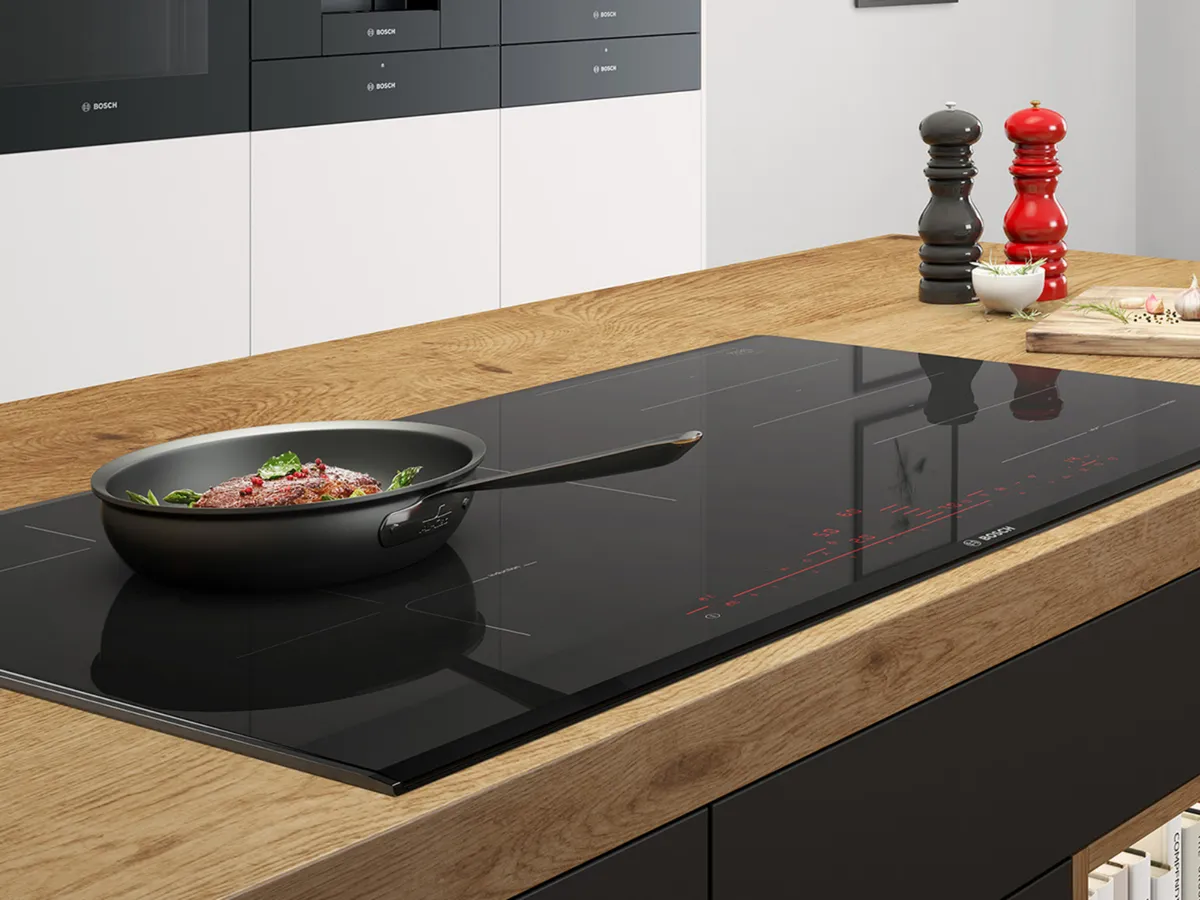 Moderne Küche mit Holzarbeitsplatte, schwarzem Induktionskochfeld und diversen Kochutensilien.