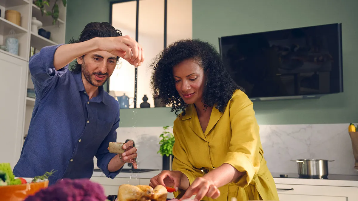 In a kitchen, a man and woman collaborate to prepare food, surrounded by various cooking tools and ingredients.