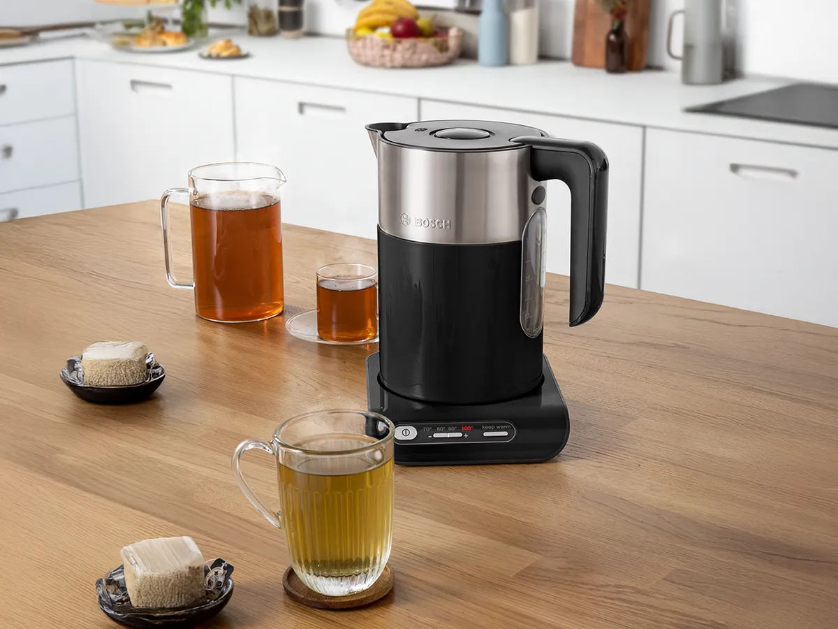 Βραστήρας Styline σε μαύρο και stainless steel πάνω σε έναν πάγκο κουζίνας, δίπλα σε διάφορα ζεστά ροφήματα σε ποτήρια.