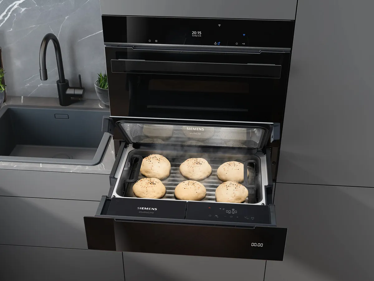 Siemens Dampfschublade mit sechs Brötchen auf einem Tablett in einer modernen Küche neben einer Spüle.