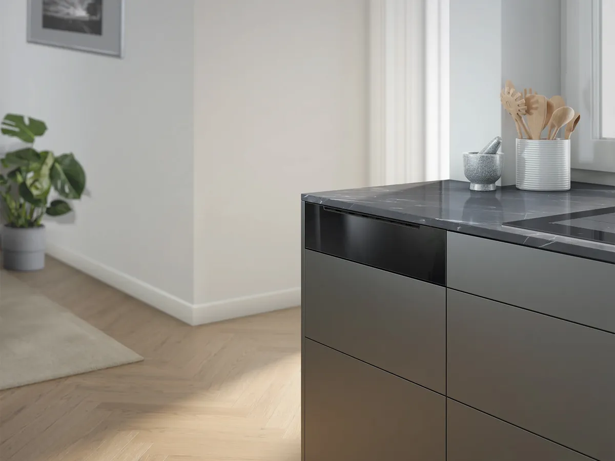 Moderne Küche mit dunkler Arbeitsplatte, Induktionskochfeld und hellem Holzfußboden. Unter der Arbeitsplatte ist eine Dampfschublade eingebaut.