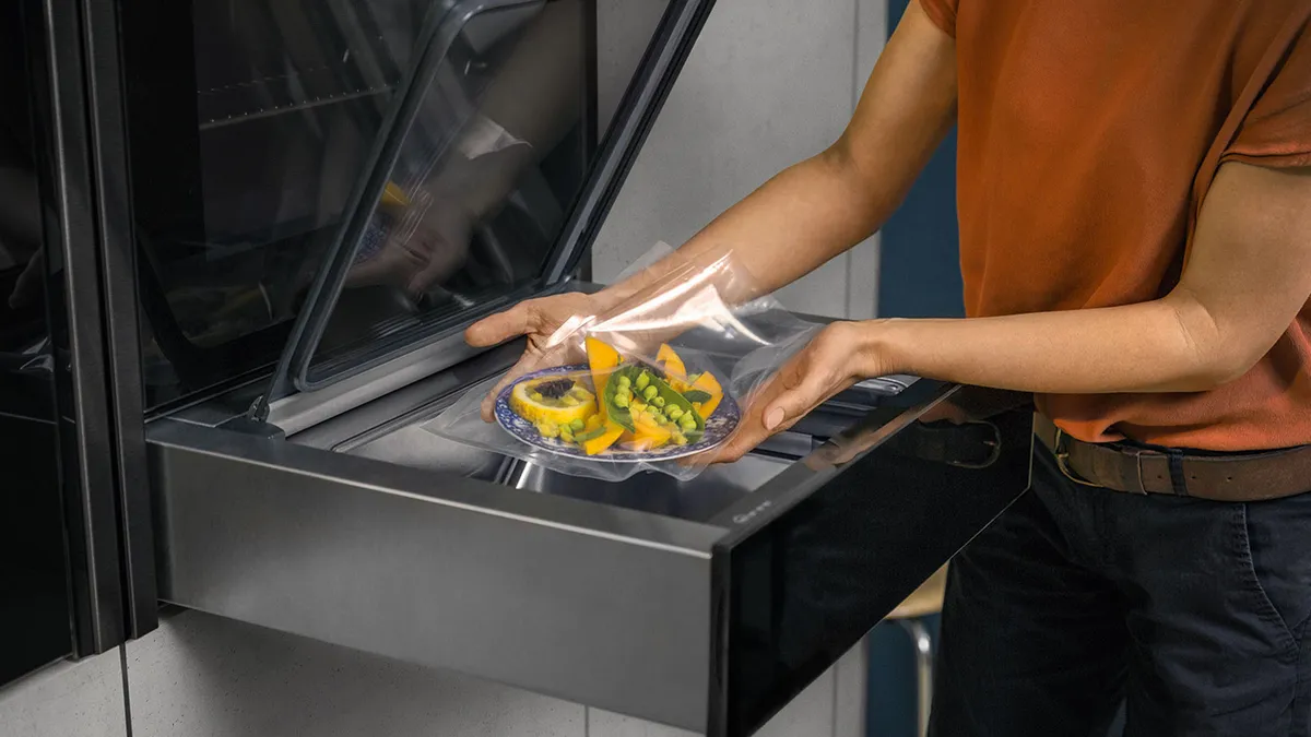  A person placing food items into an open refrigerator, organizing the contents for storage.  