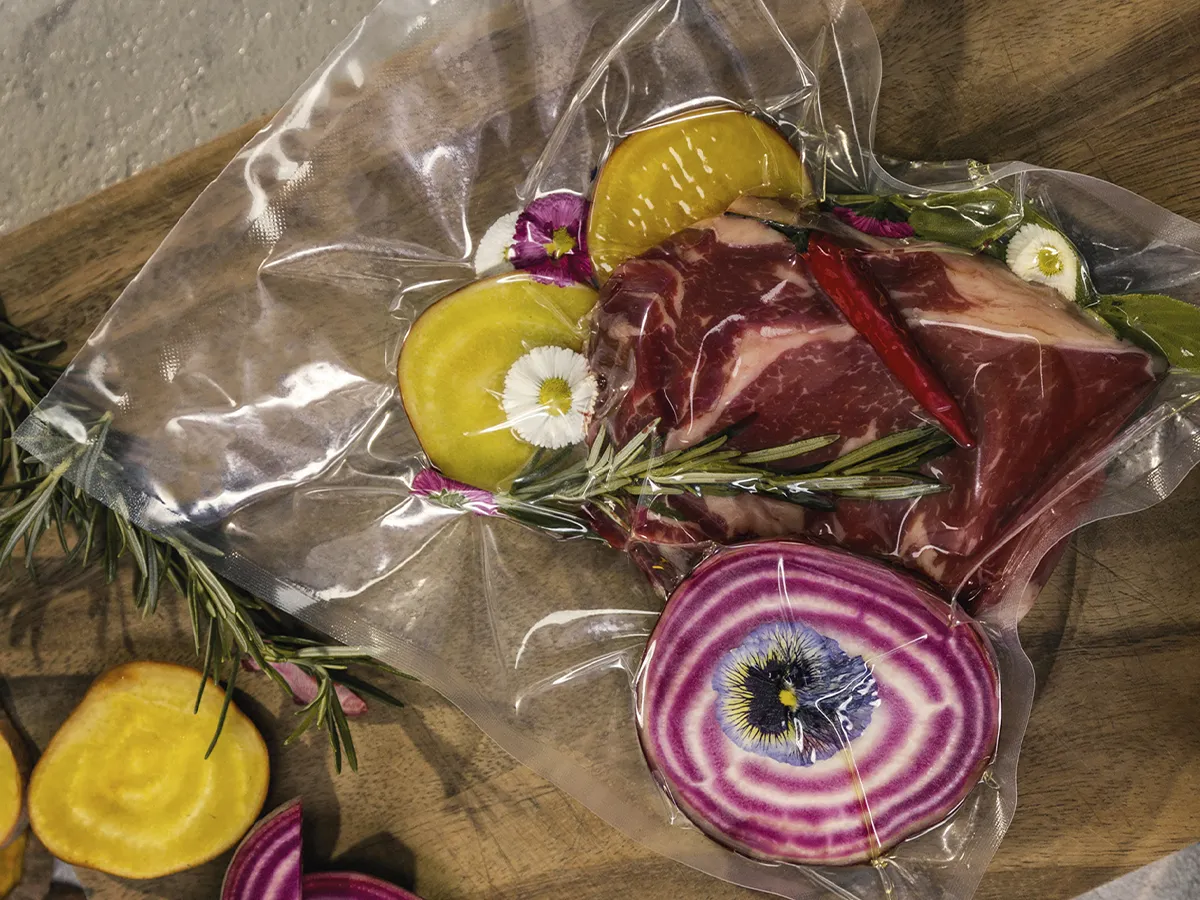 Fresh meat and various vegetables arranged in transparent plastic bags, ready for purchase or preparation.  